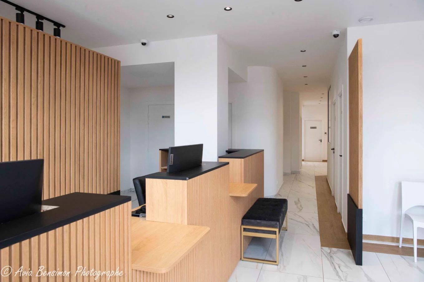 Espace d’accueil et couloir menant aux salles de soins, murs blancs et bois clair